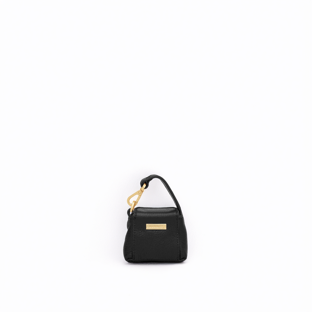 A small black textured leather handbag with a top handle, gold-tone hardware, and a gold rectangular logo plaque, centered on a plain white background.
