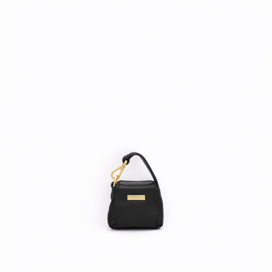 A small black textured leather handbag with a top handle, gold-tone hardware, and a gold rectangular logo plaque, centered on a plain white background.
