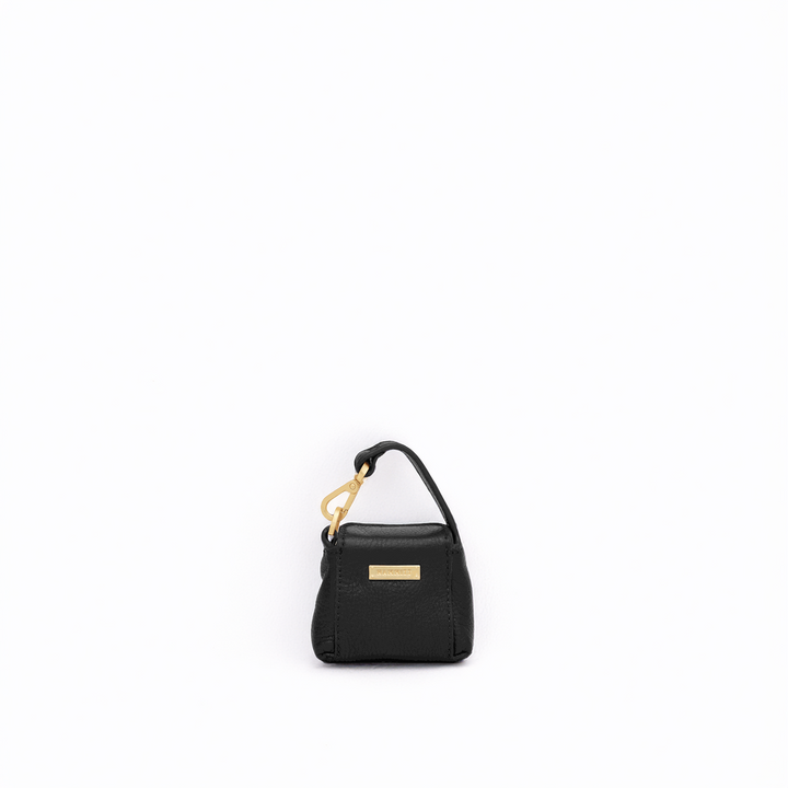 A small black textured leather handbag with a top handle, gold-tone hardware, and a gold rectangular logo plaque, centered on a plain white background.