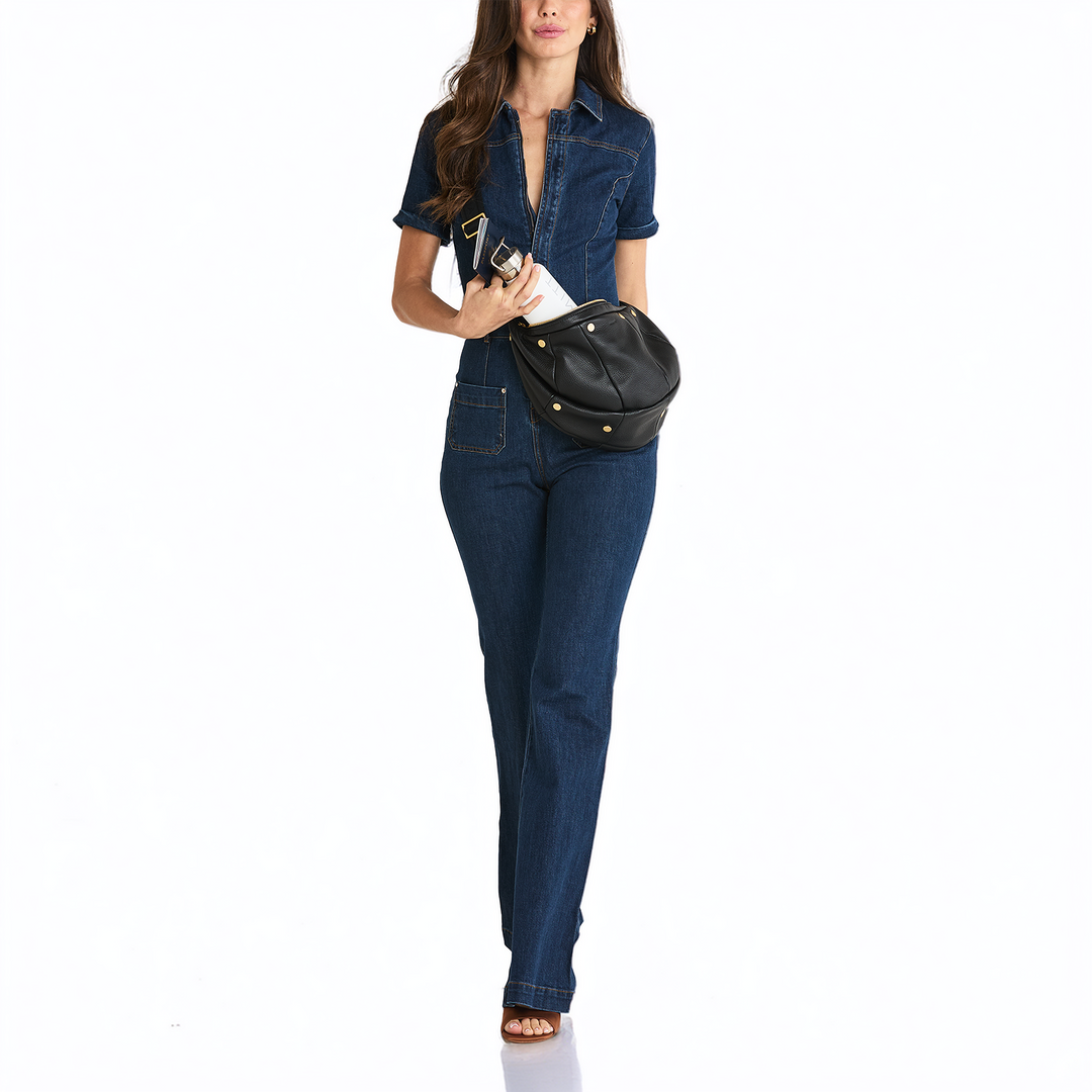 A woman modeling a dark blue denim short-sleeve shirt and matching straight-leg jeans, carrying a black faux-leather crossbody bag with gold-tone studs, against a plain white background.
