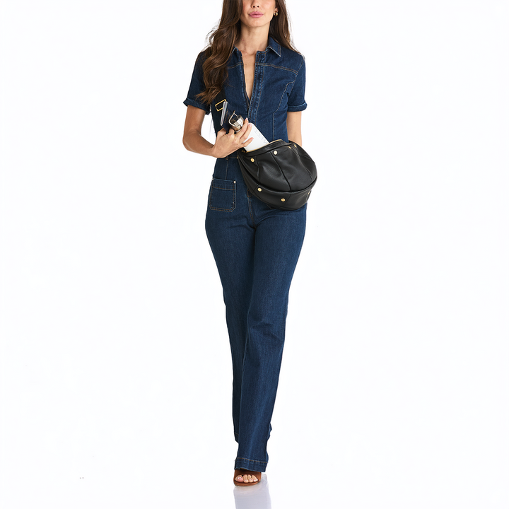 A woman modeling a dark blue denim short-sleeve shirt and matching straight-leg jeans, carrying a black faux-leather crossbody bag with gold-tone studs, against a plain white background.
