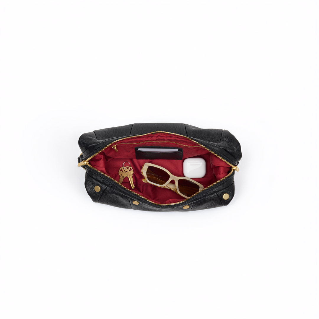 An open black leather pouch with gold-tone hardware, revealing a deep red interior. Inside, a black wallet, a pair of gold-framed sunglasses, and a white earbud case are neatly stored, all set against a clean white background.