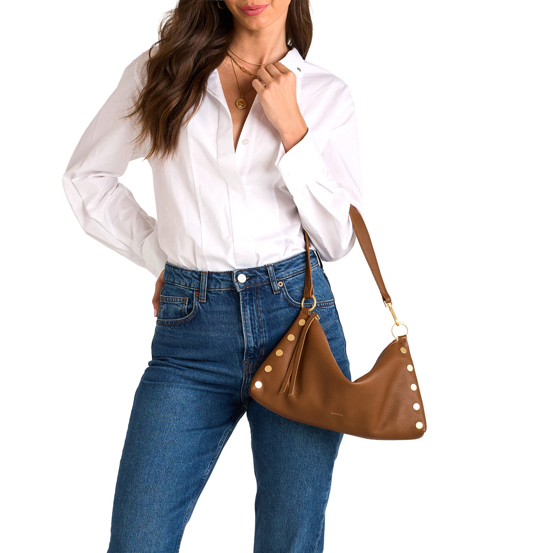 Woman wearing a white shirt and blue jeans, holding a brown handbag with white studs on a white background