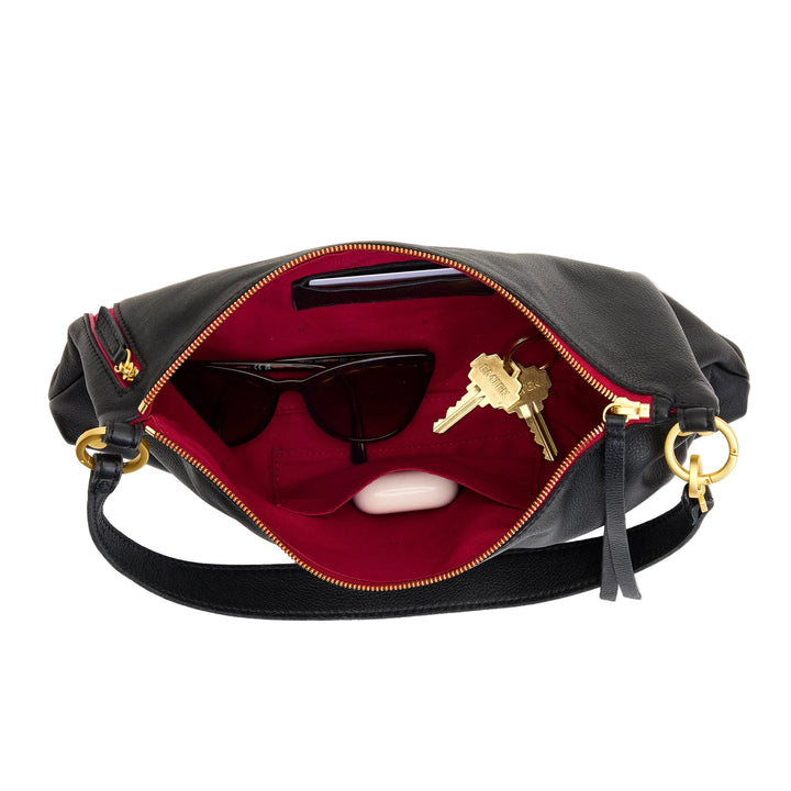 Black handbag with gold accents open on a white background, showing sunglasses, keys, and a phone.