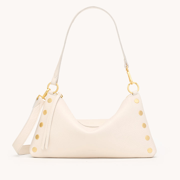 An off-white pebbled leather shoulder bag with gold-tone hardware, featuring a crescent-shaped body, a tassel detail, and a matching shoulder strap, shown against a solid off-white background.