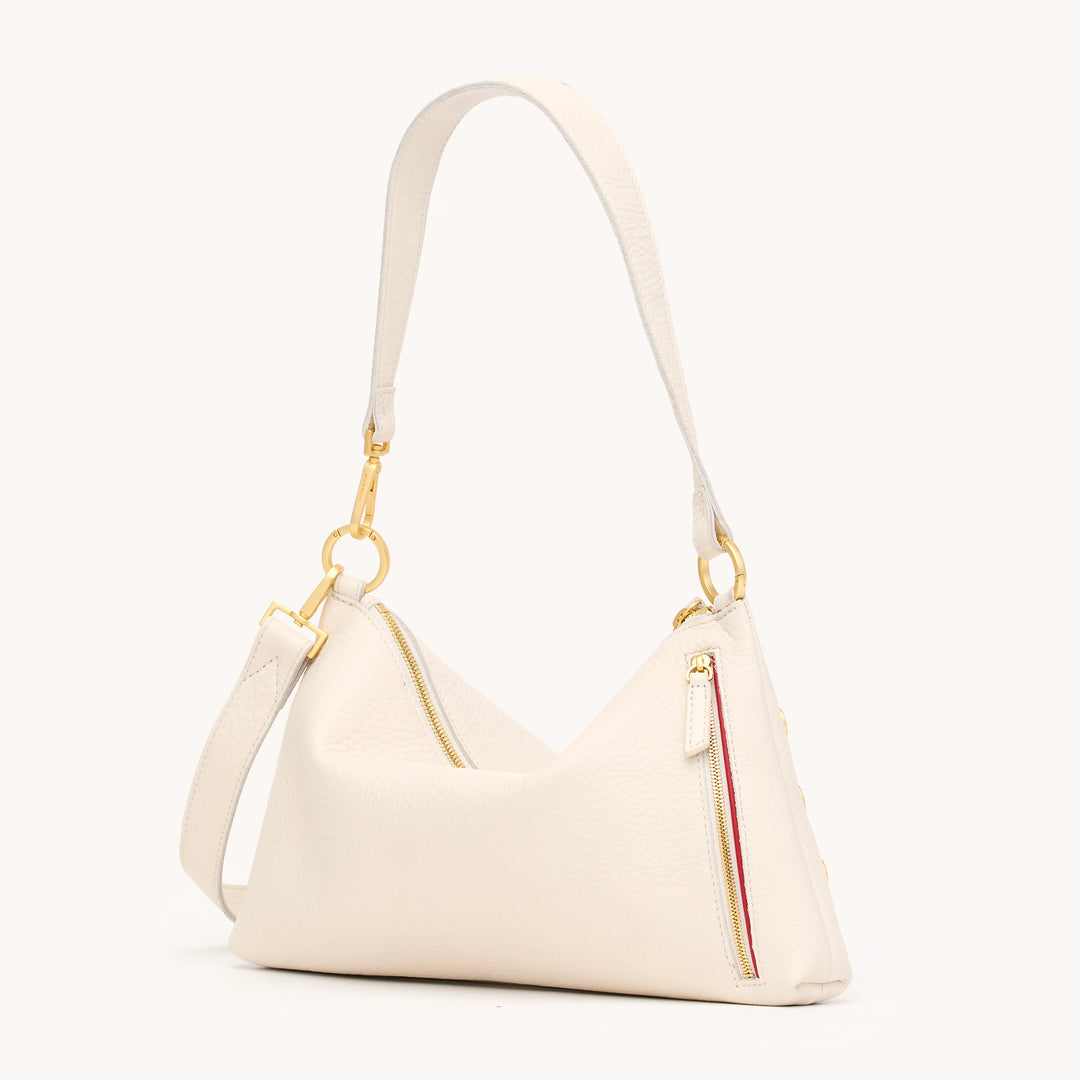 An off-white pebbled leather shoulder bag with gold-tone hardware, featuring a zippered main compartment, a zippered side pocket with a red and yellow stripe detail, and a matching adjustable shoulder strap, shown against a plain off-white background.