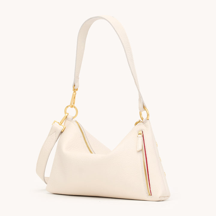 An off-white pebbled leather shoulder bag with gold-tone hardware, featuring a zippered main compartment, a zippered side pocket with a red and yellow stripe detail, and a matching adjustable shoulder strap, shown against a plain off-white background.
