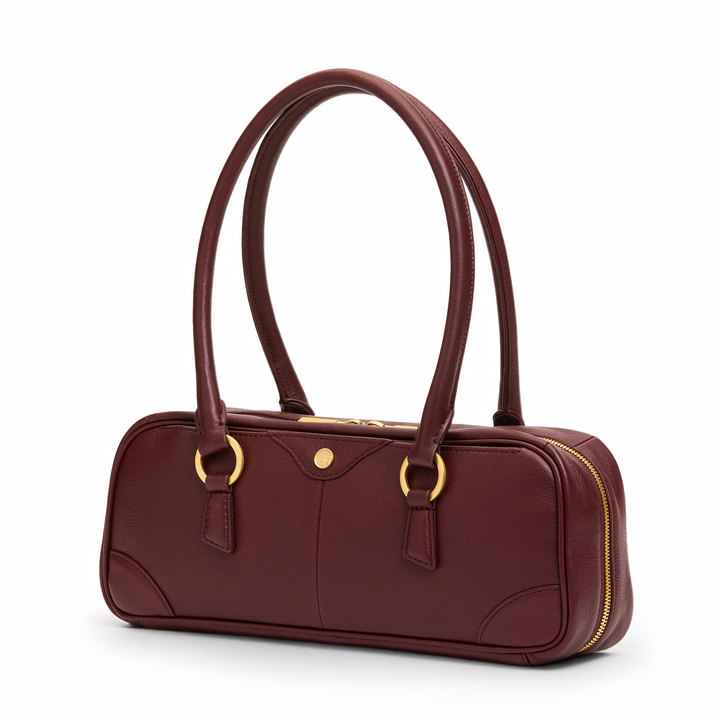 A burgundy leather handbag with gold-tone hardware, featuring dual top handles, a zippered closure, and a small round gold button on the front, set against a plain white background.