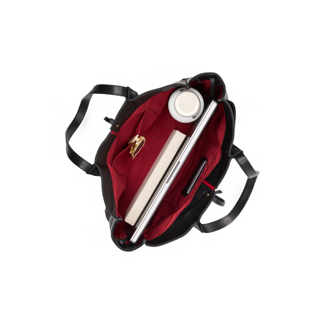 An open black tote bag with a deep red interior, shown from a top-down view on a white background. The bag is styled with a silver laptop, a white mug, and a notebook inside.