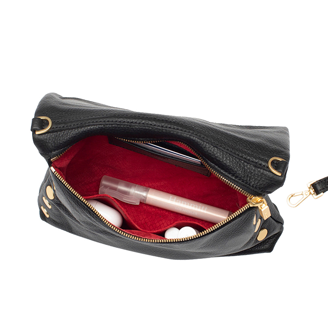 A black pebbled leather cosmetic pouch shown open, revealing a bright red interior lined with a matching red fabric organizer. The pouch has gold-tone hardware, including a zipper, grommets, and a wrist strap attachment, and contains various makeup items.