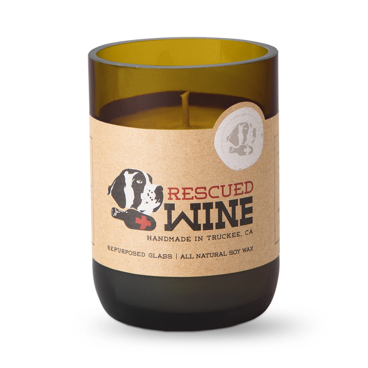 A candle in a repurposed amber glass wine bottle with a kraft paper label that reads &