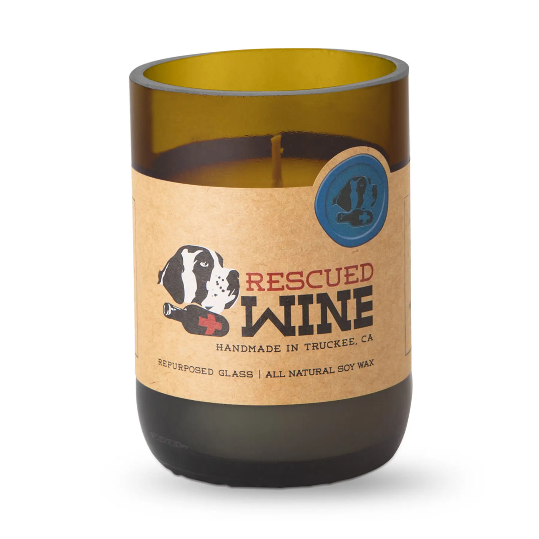 A candle in a repurposed amber glass wine bottle with a kraft paper label that reads &