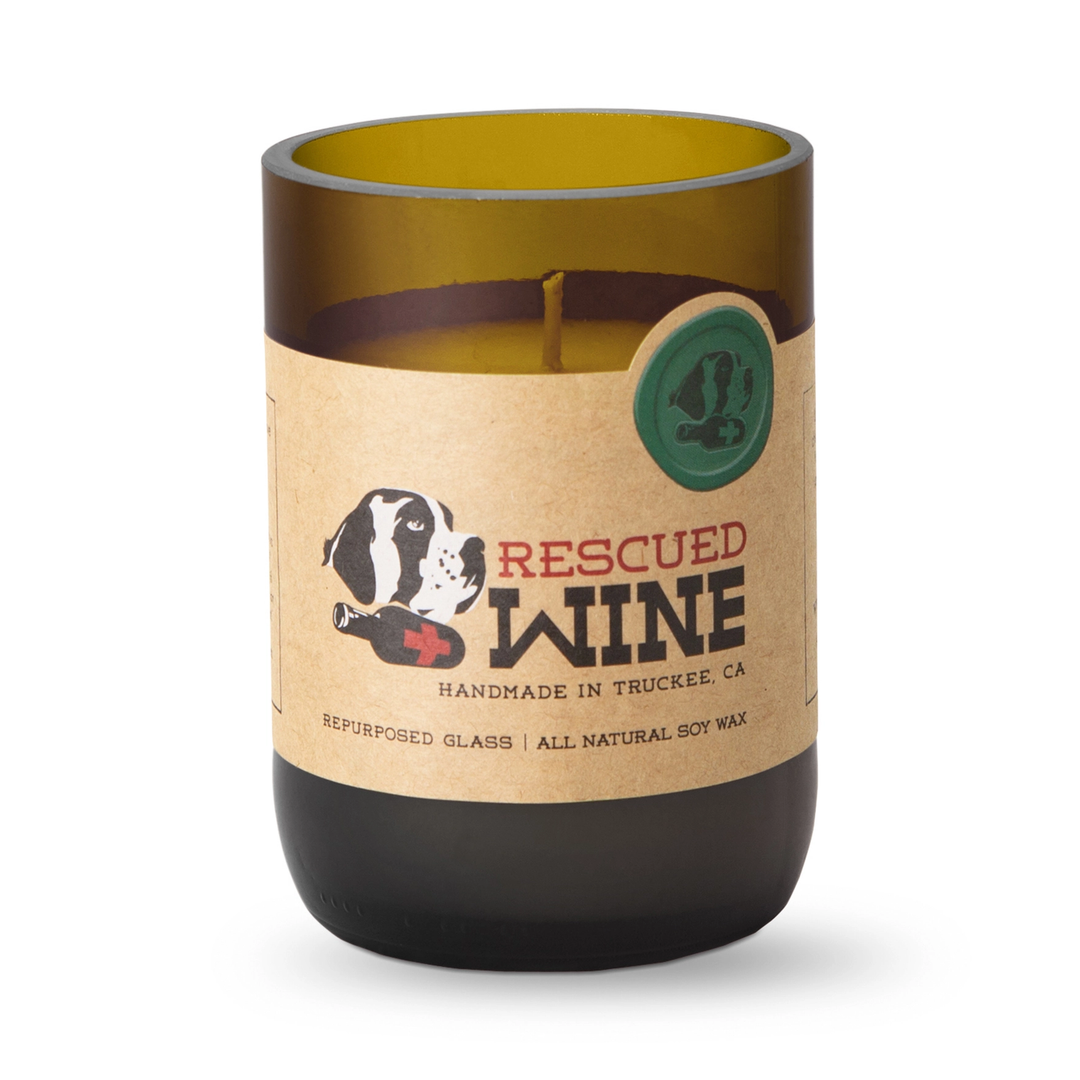 A candle in a repurposed amber glass wine bottle with a kraft paper label that reads &