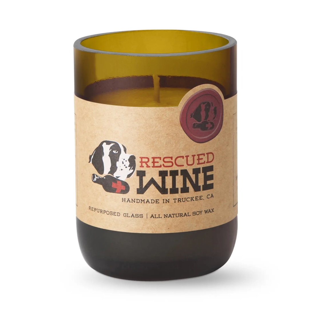 A repurposed glass candle in an olive green wine bottle shape with a kraft paper label that reads &
