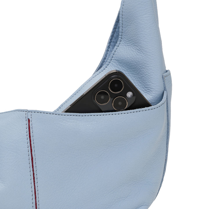 A close-up of a light blue leather shoulder bag with a black smartphone tucked into its side pocket, showing the phone&